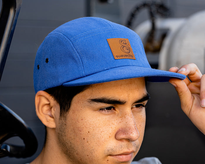 man wearing - blue suavecito hat with black text and brown background "S suavecito"