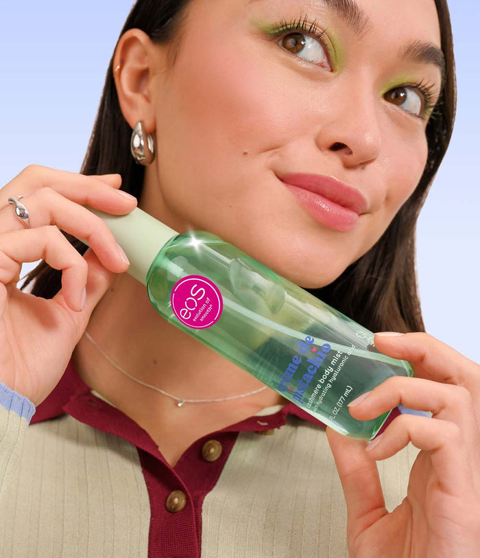 Woman holding a bottle of eos body mist with a light blue background