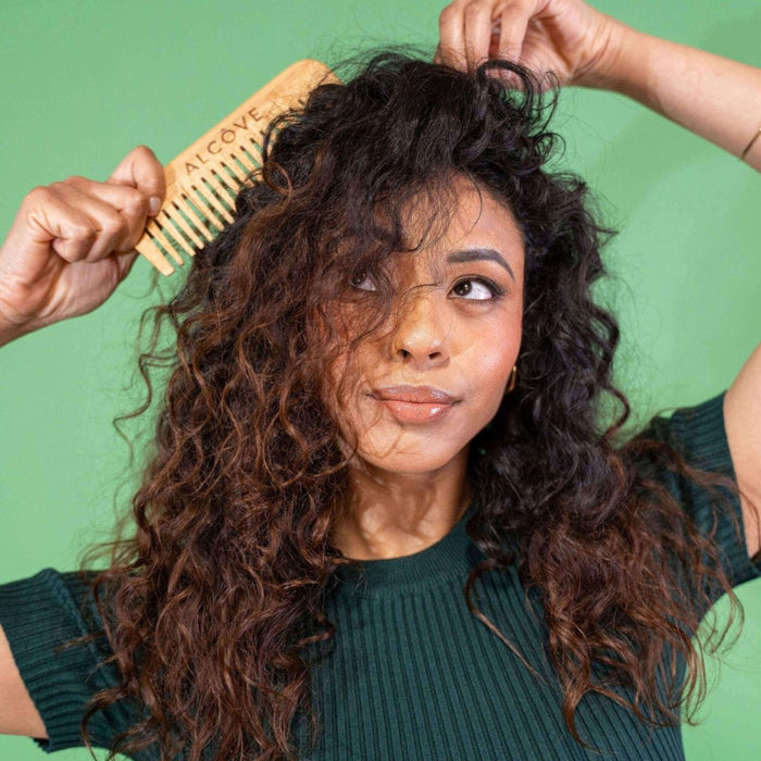 Woman combing her curly hair against a green background