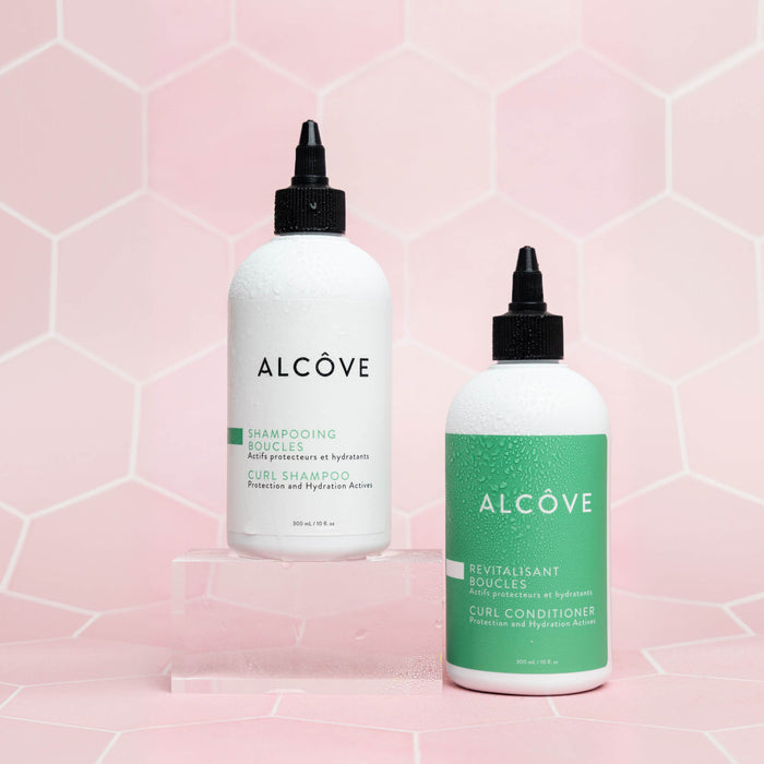 Two bottles of Alcove hair care products on a pink geometric patterned background