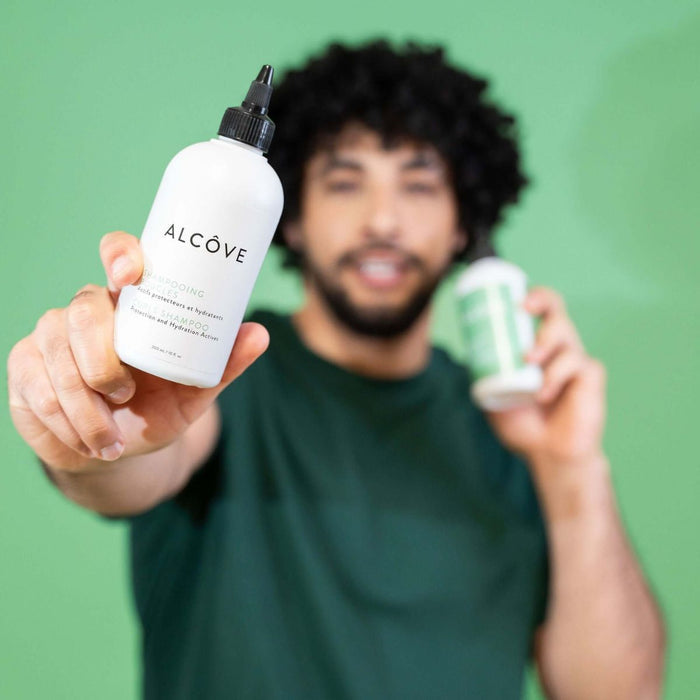 Man holding two bottles of Alcove Hair Curl Shampoo and Conditioner against a green background