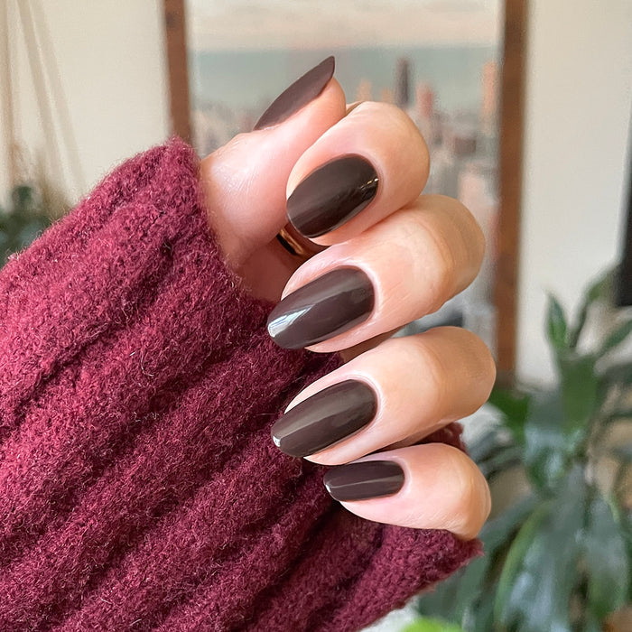 Hand with Dark Chocolate nail polish on medium-length almond-shaped nails against cozy burgundy sweater background