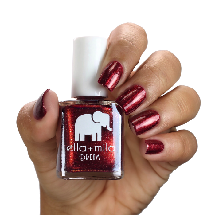 Dorothy's Stilettos deep red shimmer nail polish on a medium skin tone, hand holding the bottle
