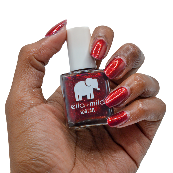 Dorothy's Stilettos deep red nail polish on a deep skin tone, hand holding the bottle