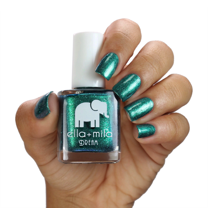 Emerald Memories dark green shimmer nail polish on a medium skin tone, hand holding the bottle