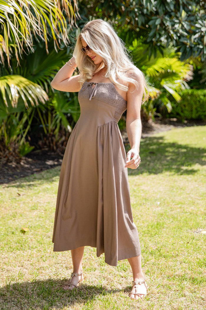 Woman in a brown dress standing in a grassy area with greenery