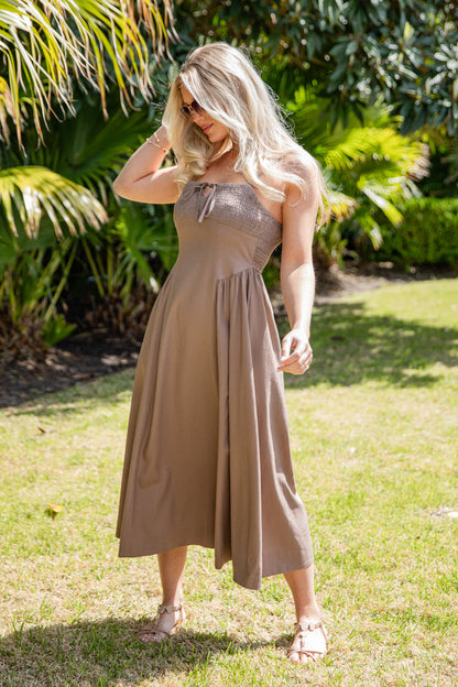 Woman in a brown dress standing in a grassy area with greenery