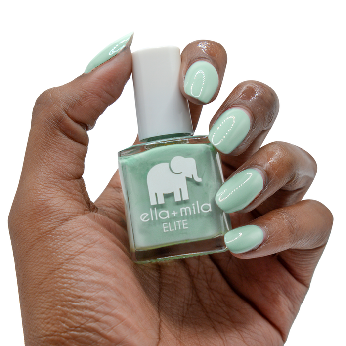 First Class icy green nail polish on a deep skin tone, hand holding the bottle