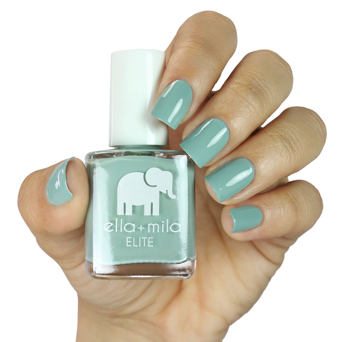 First Class muted icy green nail polish on a medium skin tone, hand holding the bottle