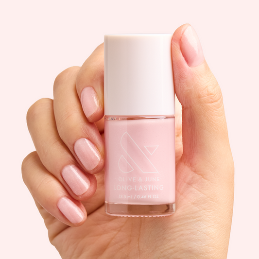 Hand holding LONG-LASTING polish bottle with nails painted in FIRST DATE sheer milky pink with silver shimmer manicure