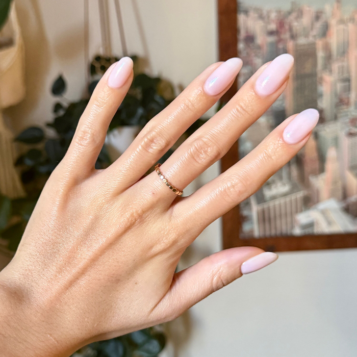 Hand with almond-shaped nails painted in FIRST DATE sheer milky strawberry pink with ultra fine silver glitter manicure