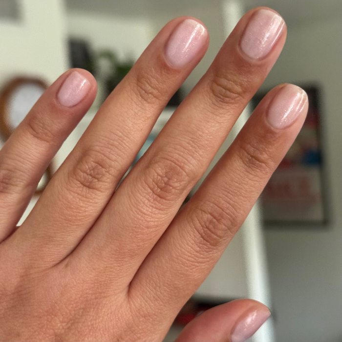 Hand with short nails painted in FIRST DATE sheer milky strawberry pink with delicate silver glitter manicure