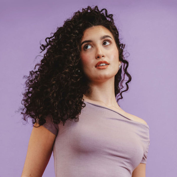 Woman with curly hair wearing a light purple top against a purple background