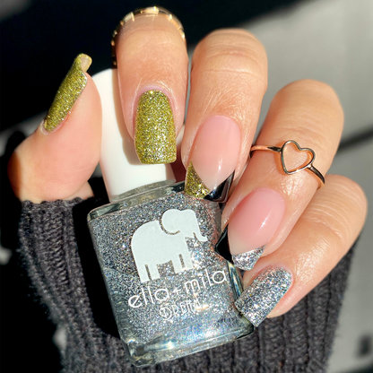 Mirage gold and silver glitter mix-and-match manicure with a heart ring, holding a glitter bottle