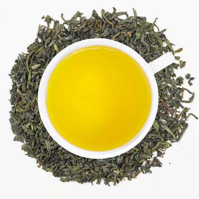 A cup of freshly brewed Organic China Green tea, surrounded by tea leaves.
