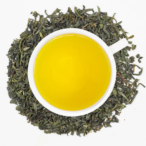A cup of freshly brewed Organic China Green tea, surrounded by tea leaves.