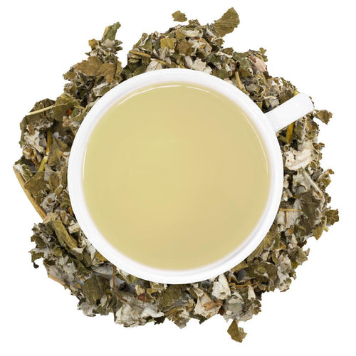 A white mug of filled with raspberry leaf tea surrounded by dried raspberry leaves