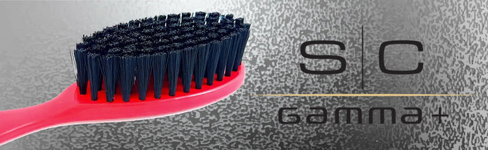A close-up of a hairbrush with a bright pink-red handle and black bristles, shown against a textured gray background with the text 'SC Gamma+' on the right.