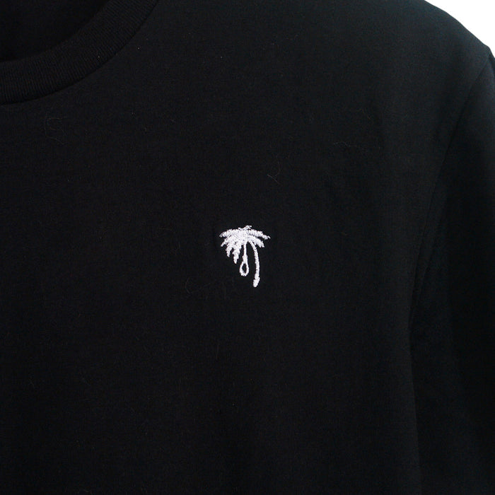 A close-up of a black Trophy Eyes shirt with a small white embroidered black palm tree on the chest—perfect for fans of subtle palm tree designs.