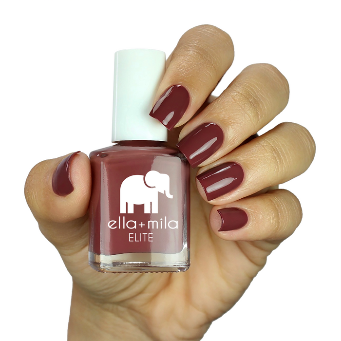 Wanderer brick red nail polish on a medium skin tone, hand holding the bottle