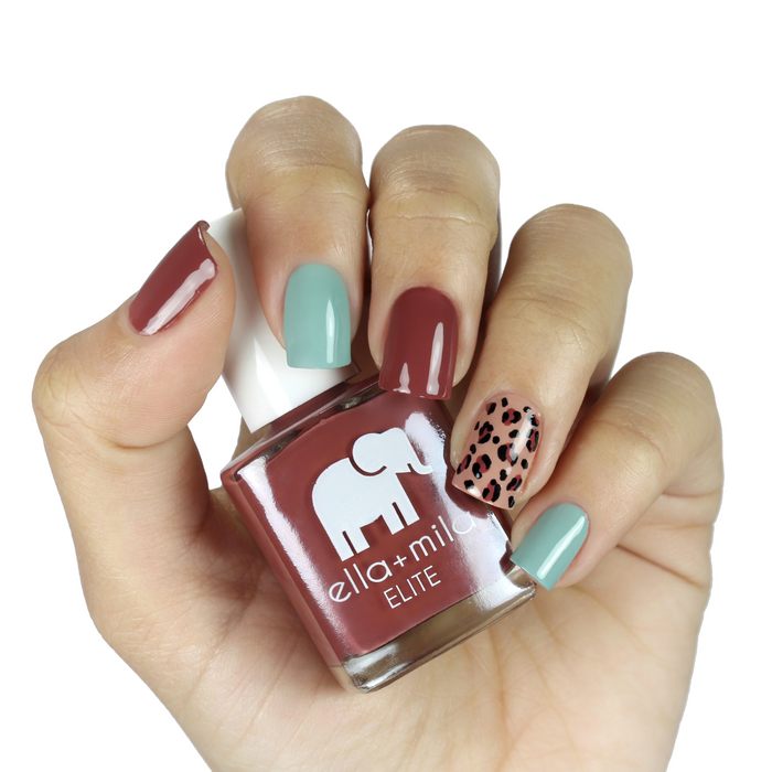 Wanderer brick red nail polish with mint and leopard-print accent nails, holding the bottle