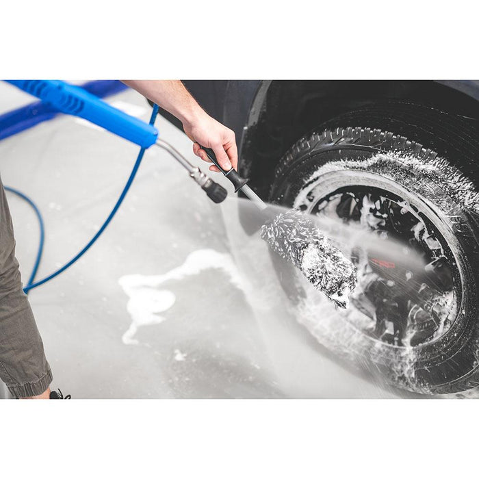 A person spraying off a wheel and Wheel brush with a blue sprayer.